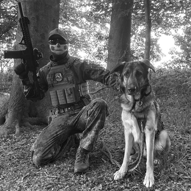 Schwarzweißaufnahme: OMUNE mit Replik und Schäferhund im Wald