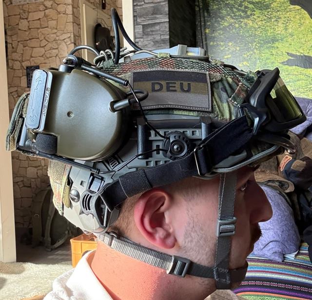 Seitenansicht eines Helms mit Flecktarn-Bezug, DEU-Patch, Headset und Schutzbrille